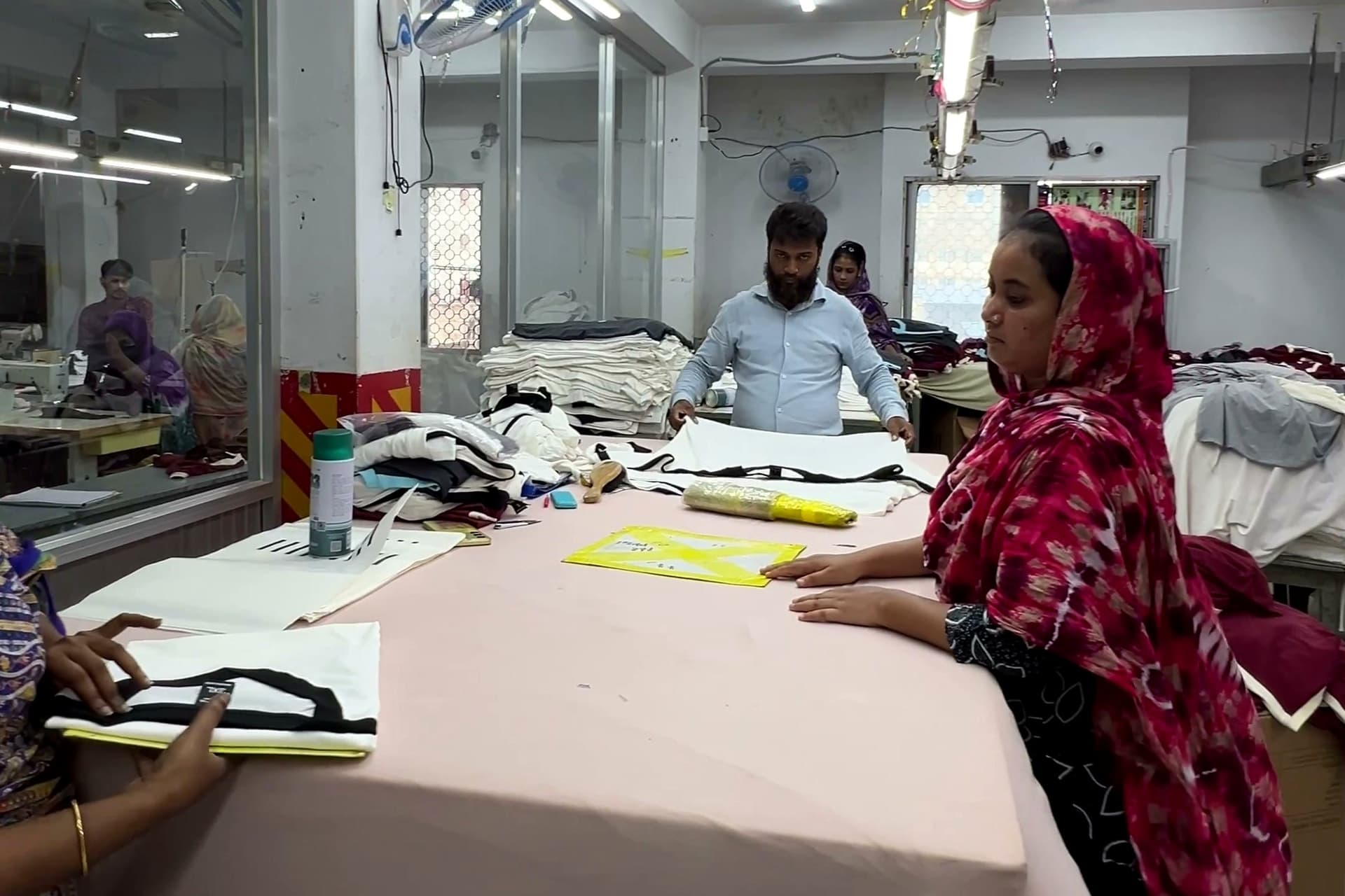 Finish-Abteilung einer Bekleidungsfabrik in Narayanganj: Mitarbeiterinnen prüfen und falten Kleidungsstücke an einem langen Tisch, dahinter Bügeltische