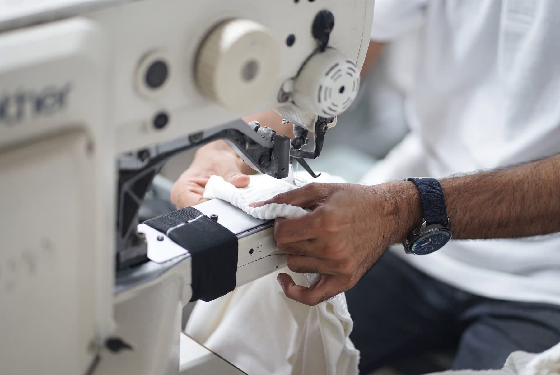 Close-up of hands guiding white fabric through an industrial sewing machine