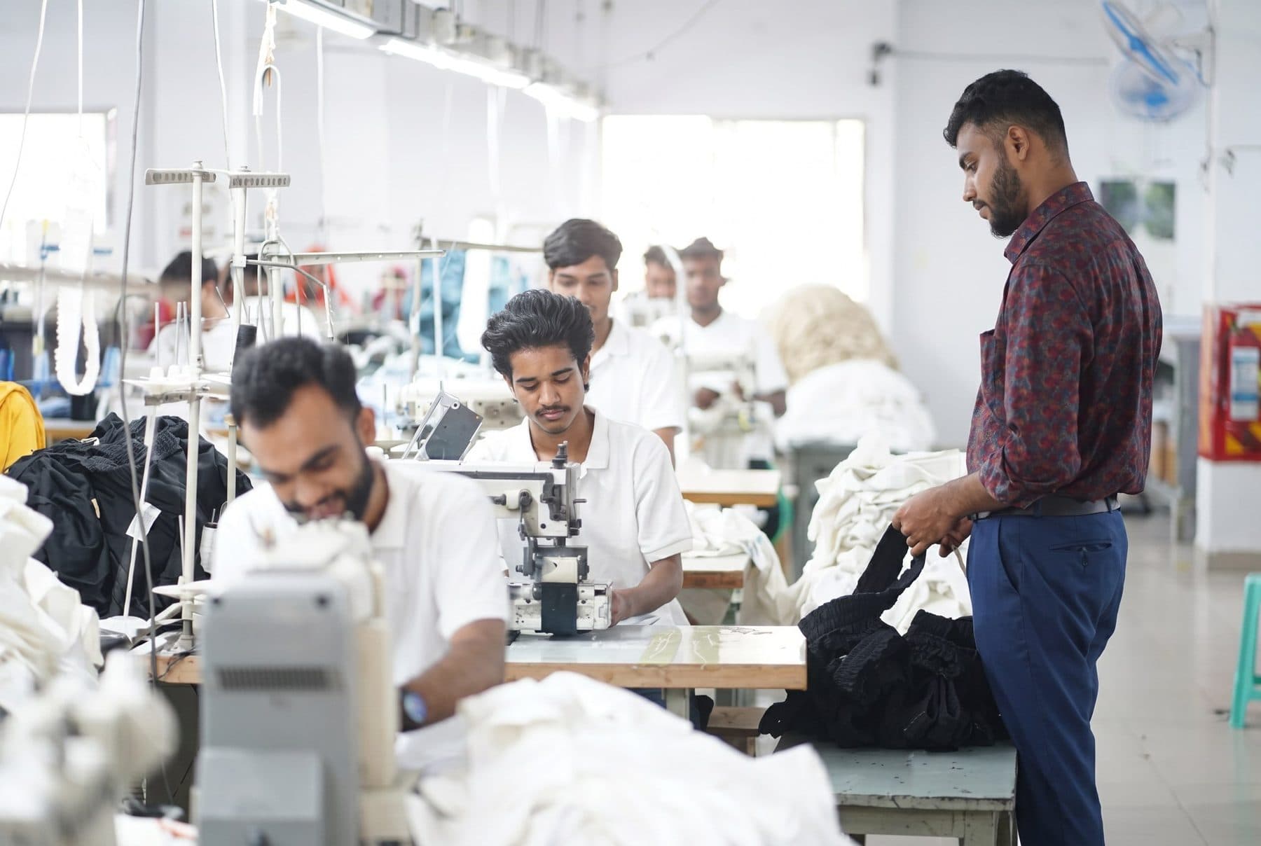 Sewing line in a Narayanganj garment factory, with operators at their machines and a supervisor checking the work